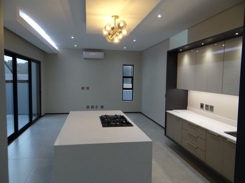 Modern, minimalist kitchen featuring a large central island with a gas hob, sleek cabinetry, stone countertops, and recessed lighting in a neutral palette.