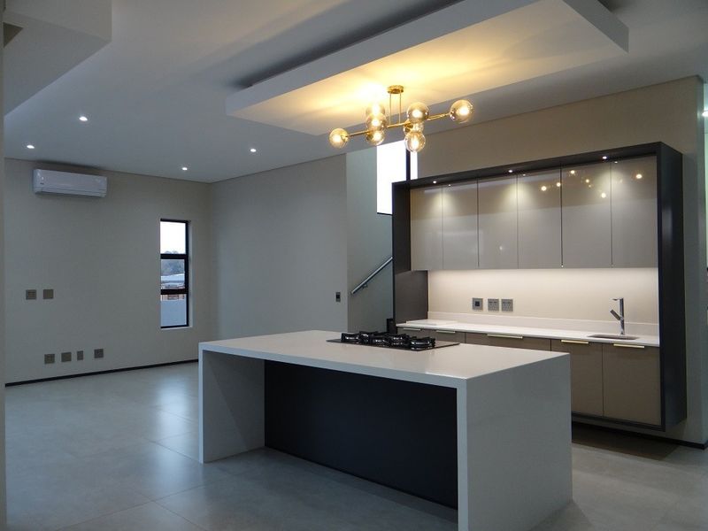 Modern open-plan kitchen featuring a central island with gas hob, sleek cabinetry, integrated lighting, and neutral porcelain floor tiles in a spacious layout.