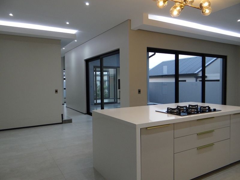 Modern open-plan living area featuring a sleek kitchen island with a gas hob, recessed ceiling lighting, and large sliding glass doors leading outdoors.