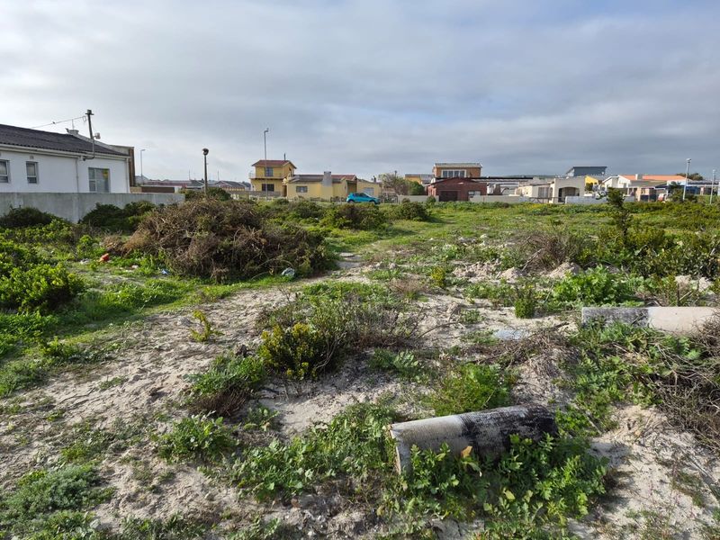 A vacant residential plot featuring sandy terrain and natural coastal vegetation, situated in an established neighborhood setting.
