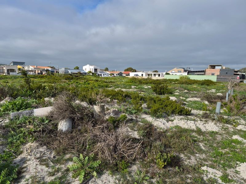 A vacant residential plot featuring natural vegetation and sandy terrain, situated in an established neighborhood with surrounding residential properties.