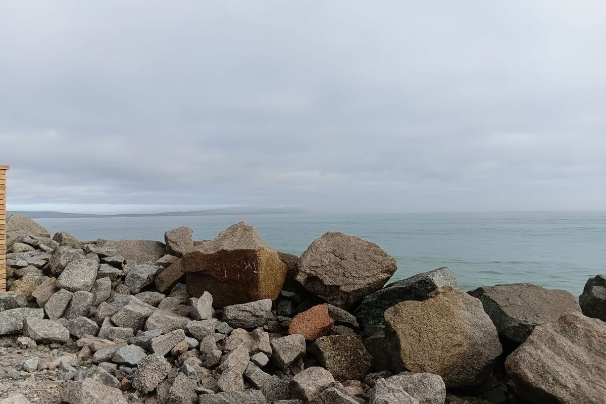 A scenic view of the ocean coastline featuring a natural rock embankment and expansive water horizon.