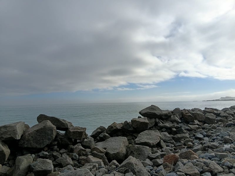 A scenic view of the ocean coastline featuring natural rock formations along the shore under a cloudy sky.