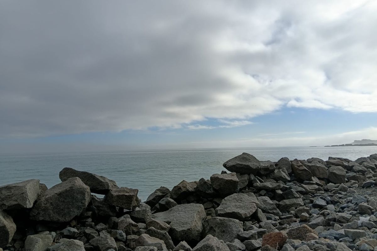 A scenic view of the ocean coastline featuring natural rock formations along the shore under a cloudy sky.