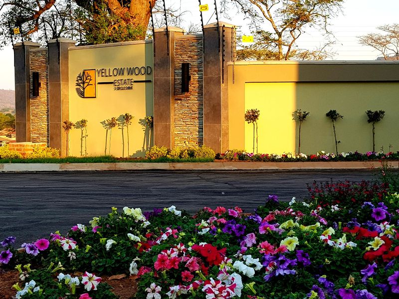 The entrance to Yellow Wood Estate featuring stone-clad pillars, electric fencing, and well-maintained landscaped garden beds.