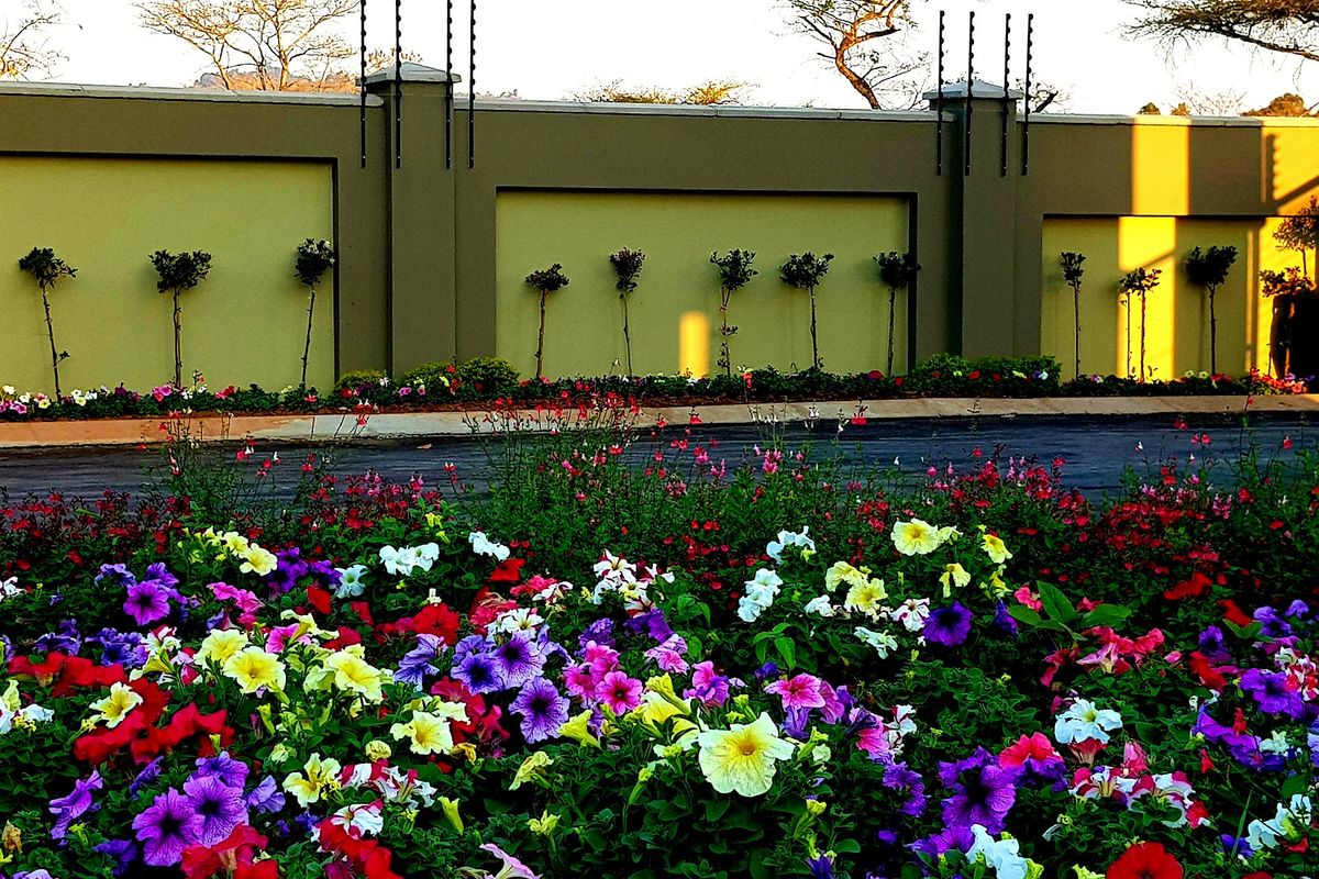 A well-maintained garden area featuring a paved driveway, perimeter wall with integrated electric fencing, and vibrant flower beds.