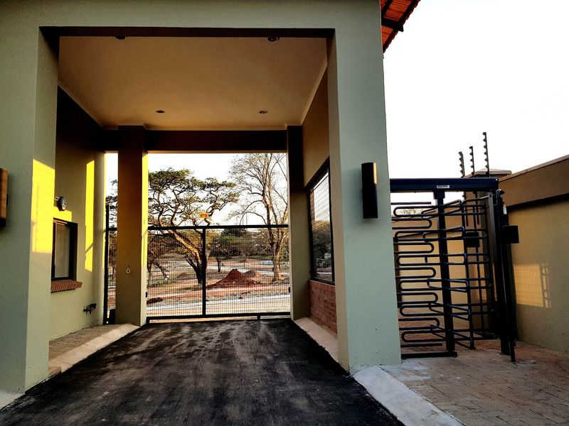 A secure gated entrance featuring a metal turnstile, electric fencing, and a paved driveway leading into the residential property.
