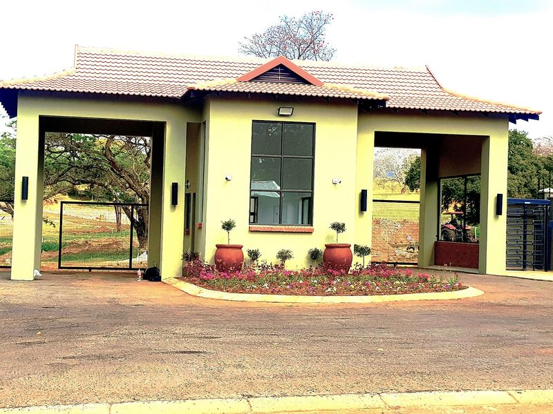 A well-maintained residential estate entrance gatehouse featuring a tiled roof, security access points, and landscaped garden beds.