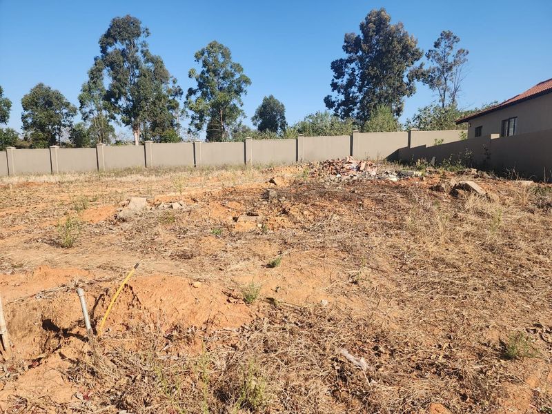A vacant residential plot featuring a perimeter wall, uneven terrain, and scattered debris, offering a blank canvas for future development.