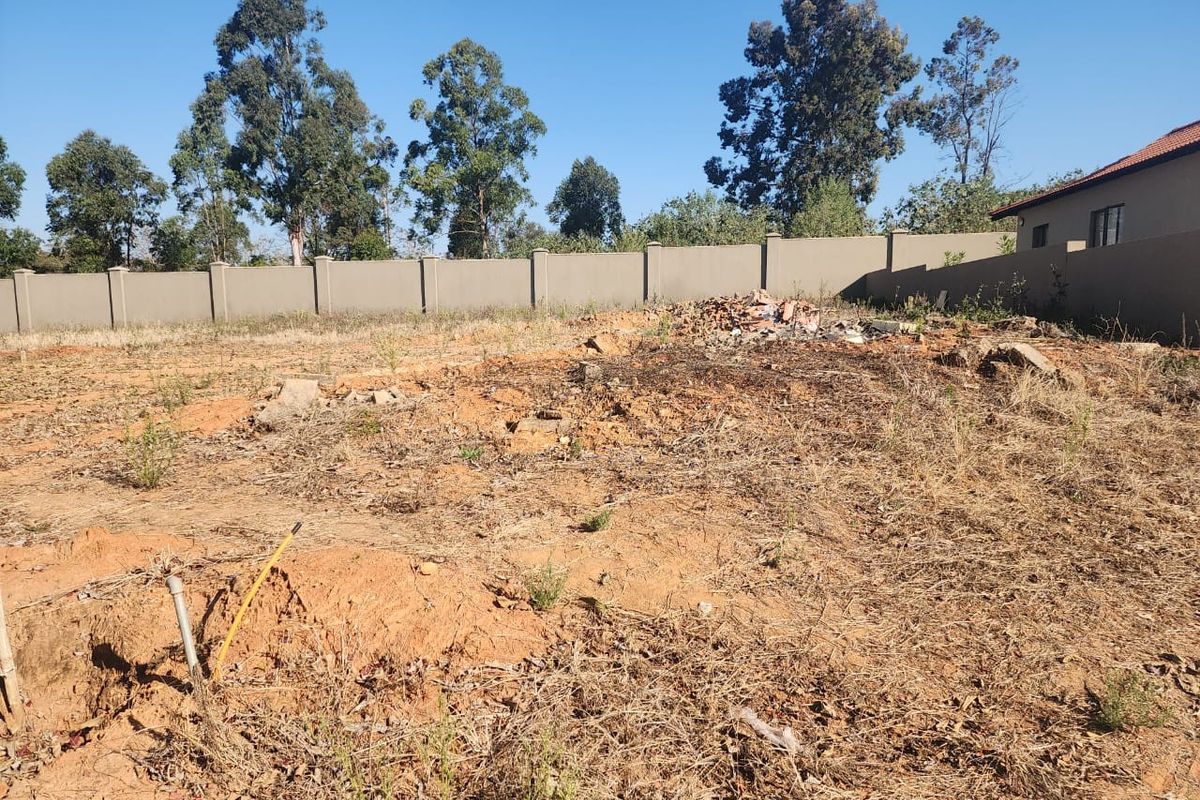 A vacant residential plot featuring a perimeter wall, uneven terrain, and scattered debris, offering a blank canvas for future development.