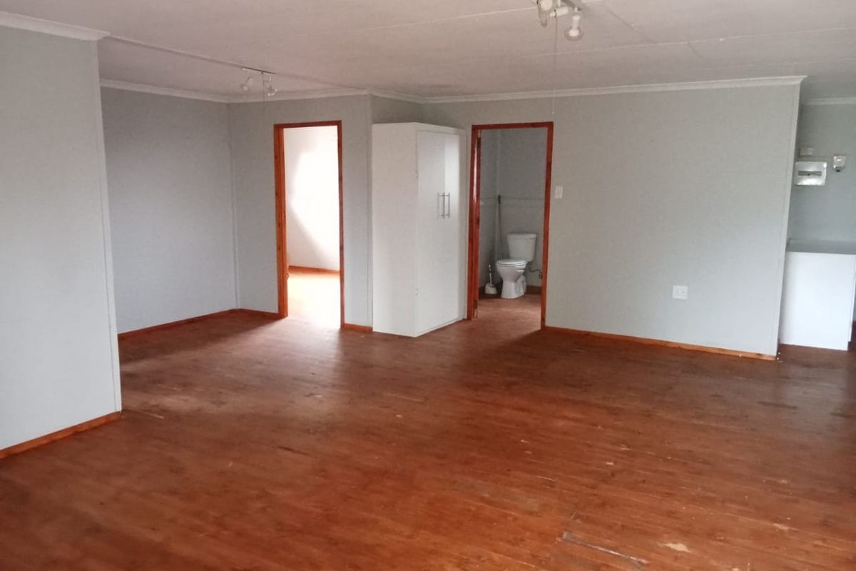 An open-plan living area featuring wooden flooring, neutral wall tones, and direct access to an adjoining bathroom and secondary room.