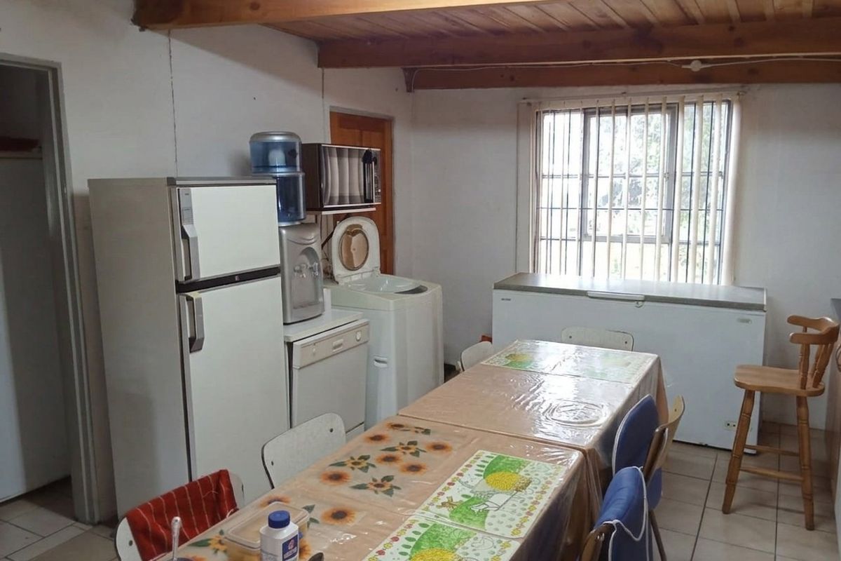 A functional kitchen area featuring exposed timber ceiling beams, tiled flooring, and a window fitted with security bars.