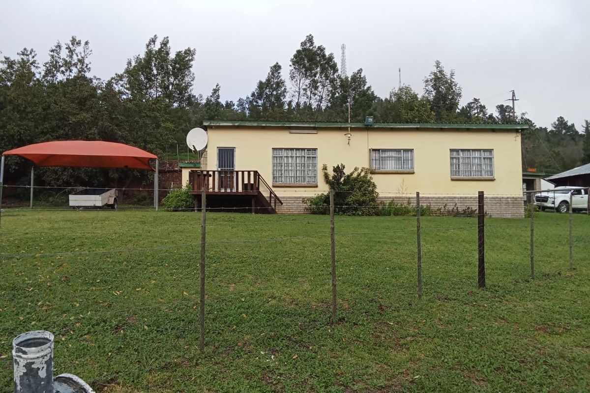 Rear view of a single-story farm dwelling featuring a timber deck, security gate, and metal roofing, set on a grassy plot.