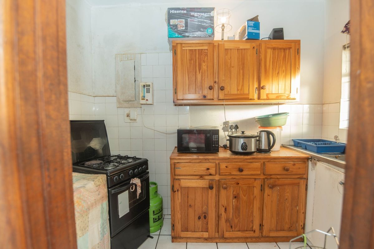 A compact kitchen featuring wooden cabinetry, a gas stove, and tiled backsplash, requiring cosmetic updates to improve its overall condition and aesthetic appeal.