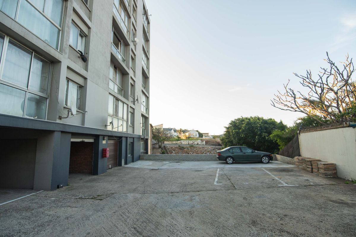 Rear exterior view of the apartment building featuring a concrete parking area and access to the garage level.