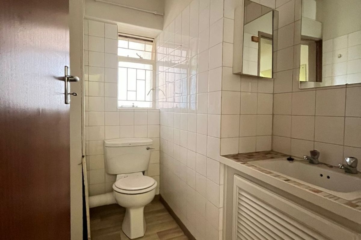 A functional bathroom featuring a vanity basin, toilet, and wall tiling, offering a clean space with potential for modern updates.