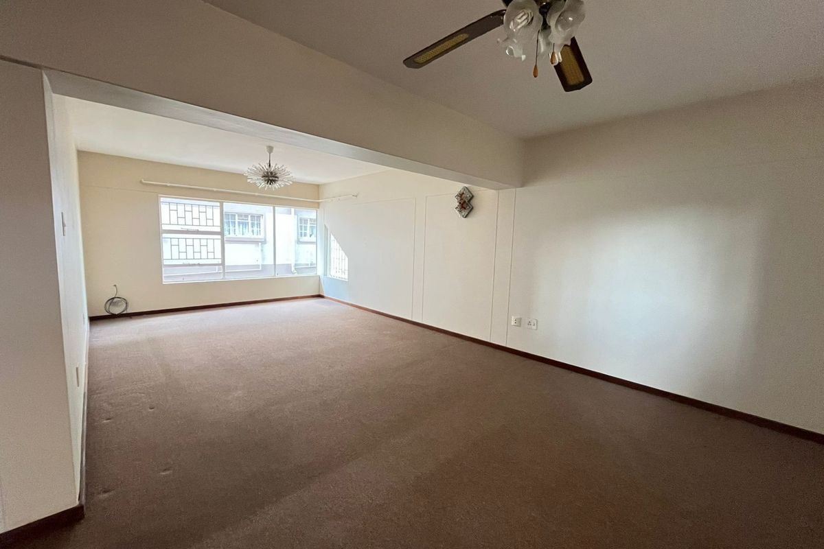 A spacious, empty living area featuring neutral carpeting, a ceiling fan, and large windows with security bars, offering a blank canvas for interior design.