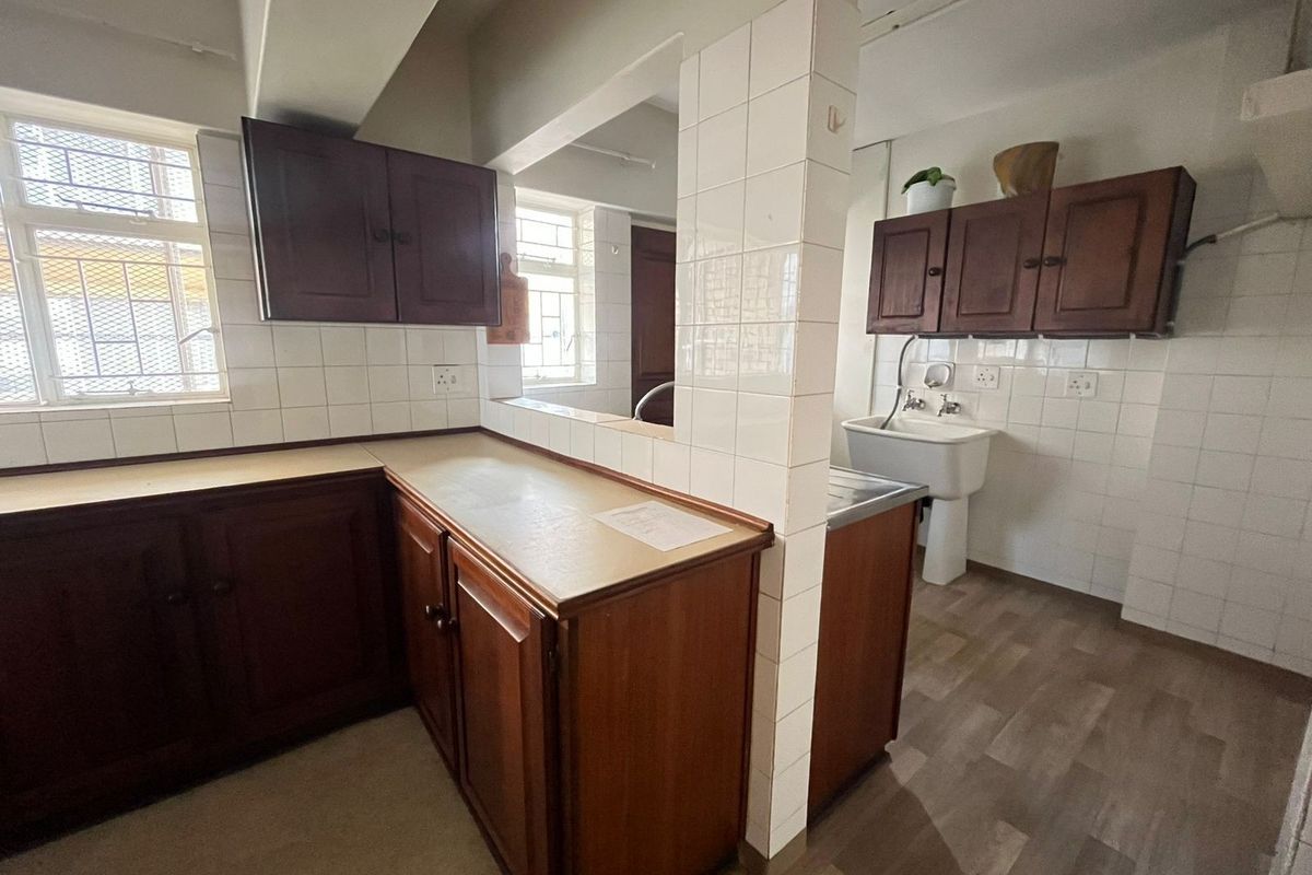 A functional kitchen area featuring built-in wooden cabinetry, laminate countertops, and a utility sink, offering a blank canvas for modern renovation.
