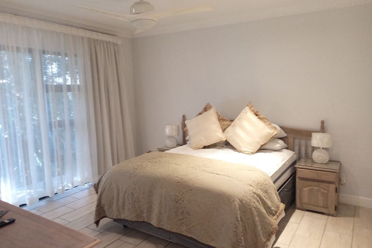 A well-lit bedroom featuring tiled flooring, a ceiling fan, and a large sliding glass door providing natural light.