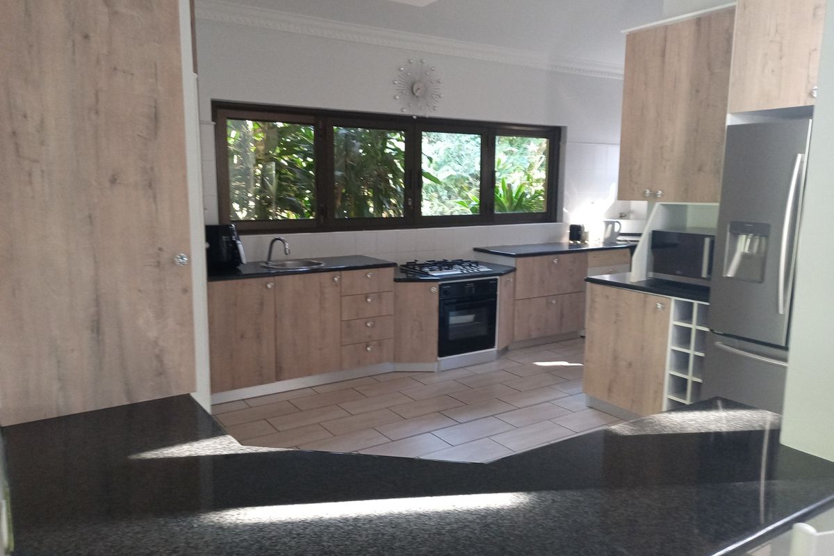 Modern kitchen featuring light wood-finish cabinetry, dark granite countertops, integrated gas hob, built-in oven, and a convenient wine rack.