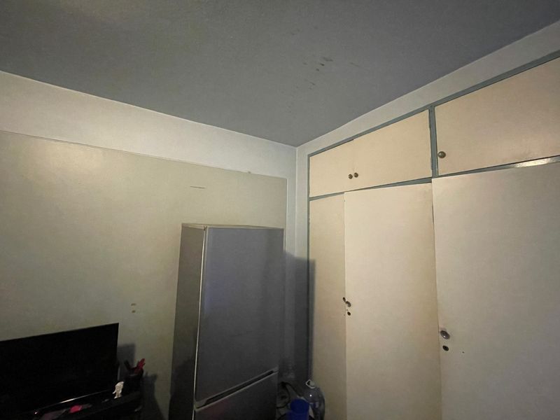 A bedroom featuring built-in storage cupboards with visible wear on the walls and ceiling, requiring cosmetic updates.