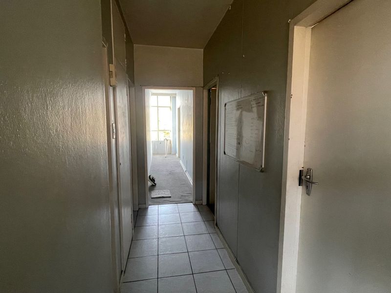 A functional apartment hallway featuring tiled flooring and multiple internal doors, leading towards a sunlit adjacent room.