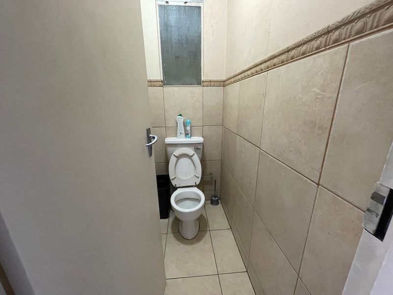 A compact bathroom featuring neutral ceramic wall and floor tiles, a standard toilet, and a small frosted glass window for natural light.