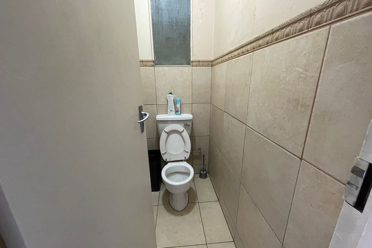 A compact bathroom featuring neutral ceramic wall and floor tiles, a standard toilet, and a small frosted glass window for natural light.