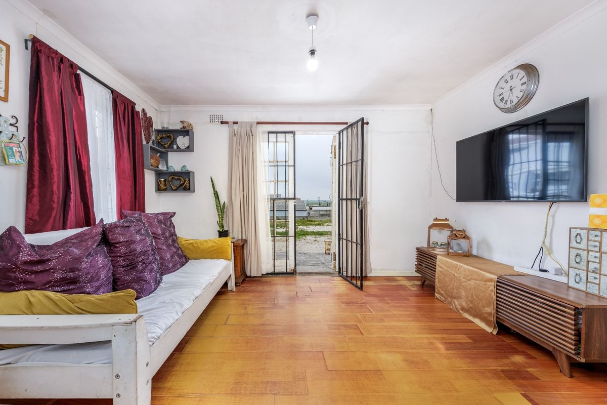 A living room featuring laminate flooring, coving, and a security gate leading to the exterior. The space requires cosmetic wall repairs.