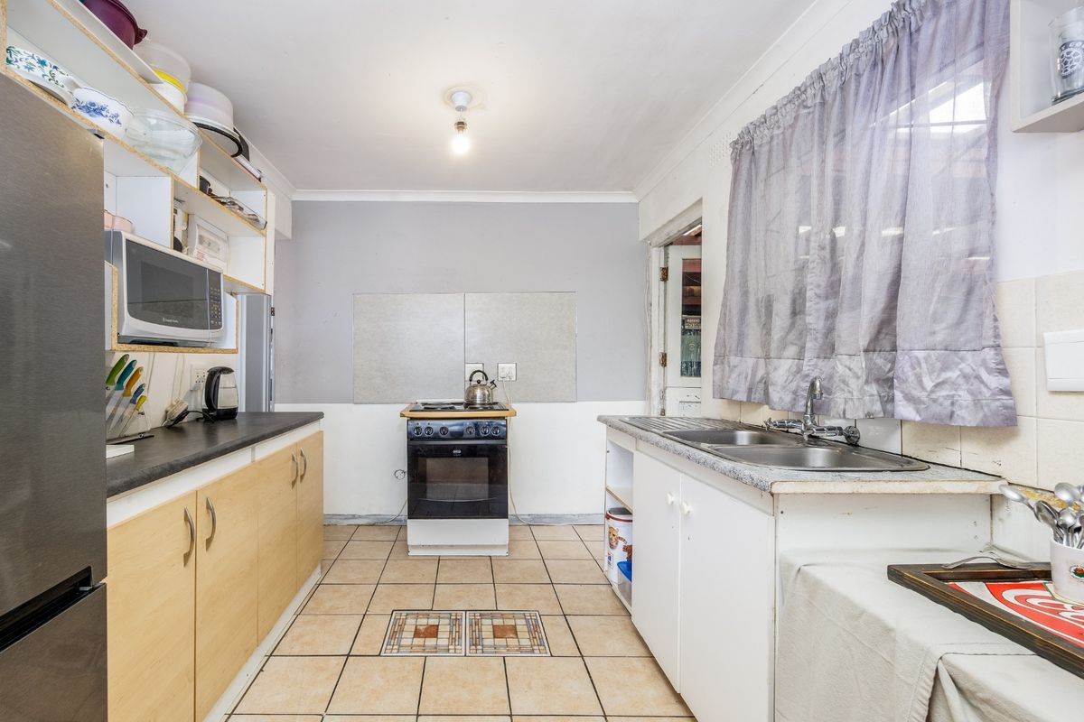 A functional kitchen featuring laminate cabinetry, a double stainless steel sink, and a freestanding oven, with ceramic tiled flooring throughout.