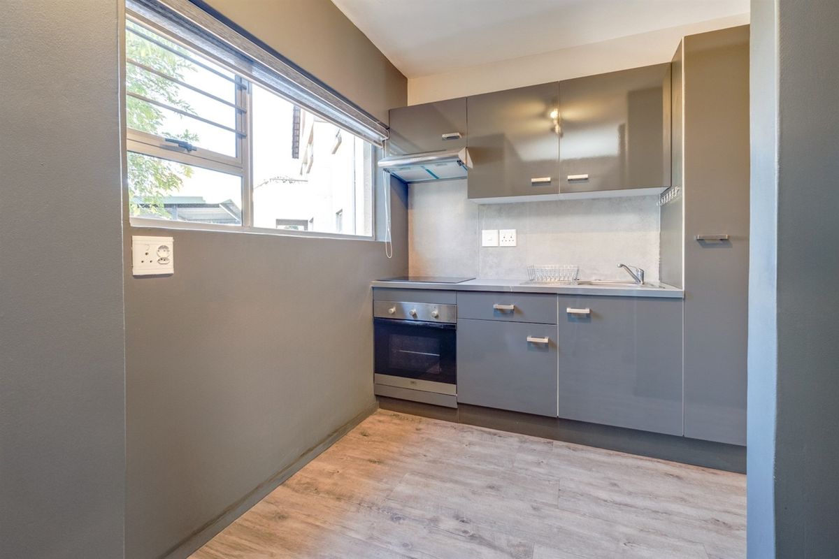 Compact modern kitchen featuring grey high-gloss cabinetry, integrated electric hob and oven, stainless steel sink, and durable laminate flooring.