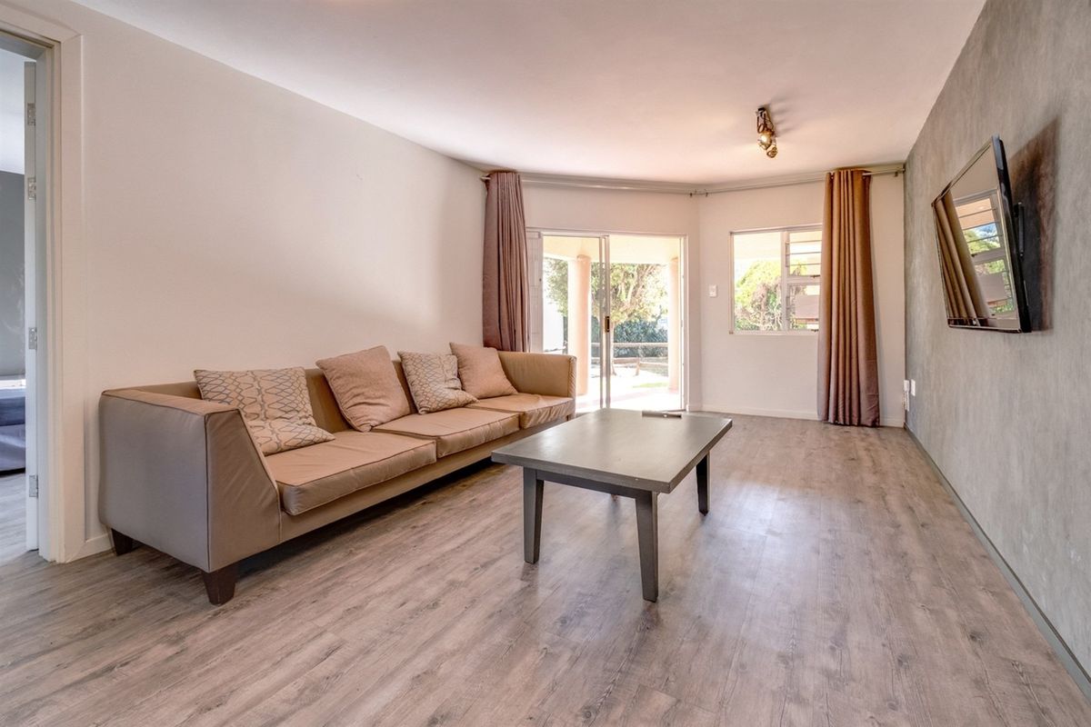 A bright living room featuring modern laminate flooring, a textured feature wall, and sliding glass doors providing access to an outdoor patio area.