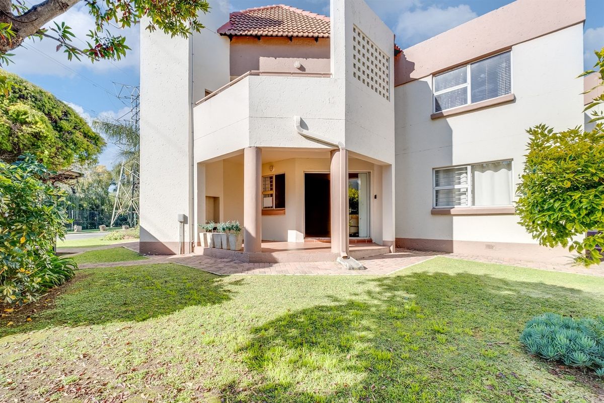 Rear view of the apartment building featuring a covered patio, brick paved walkway, and well-maintained garden area.