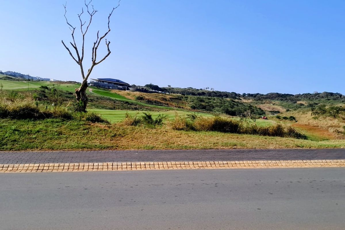 A scenic view of a vacant residential plot overlooking a golf course landscape with a paved road in the foreground.