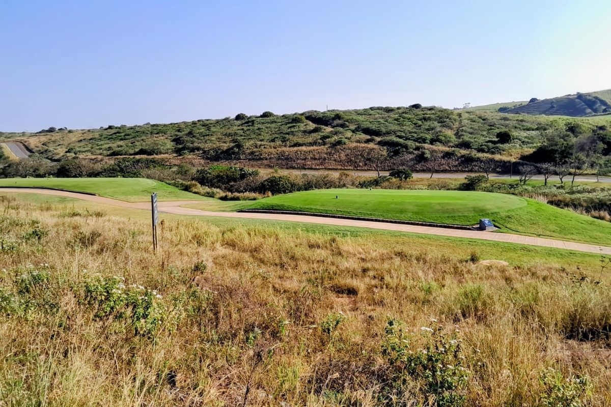 A scenic view of a manicured golf course fairway and paved cart path set against a natural hilly landscape.