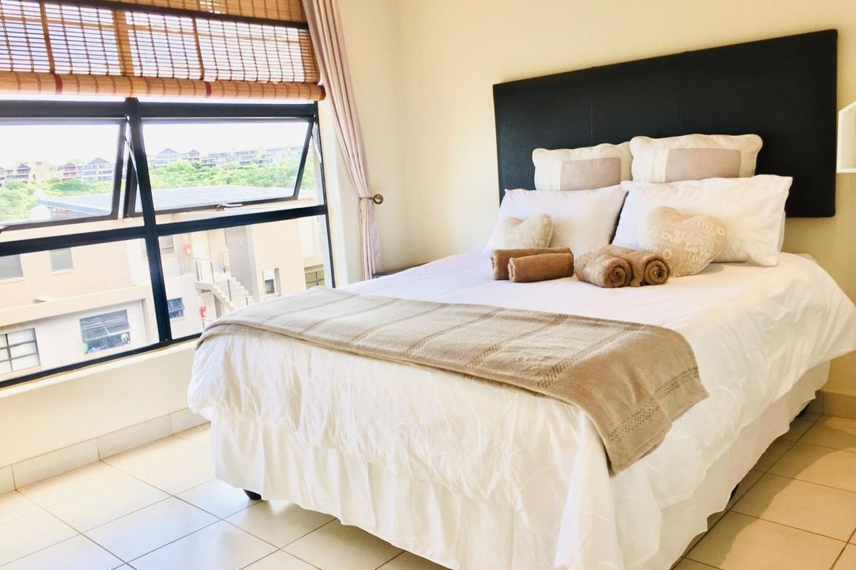 A bright bedroom featuring tiled flooring and a large window with a bamboo blind, offering natural light and an exterior view.