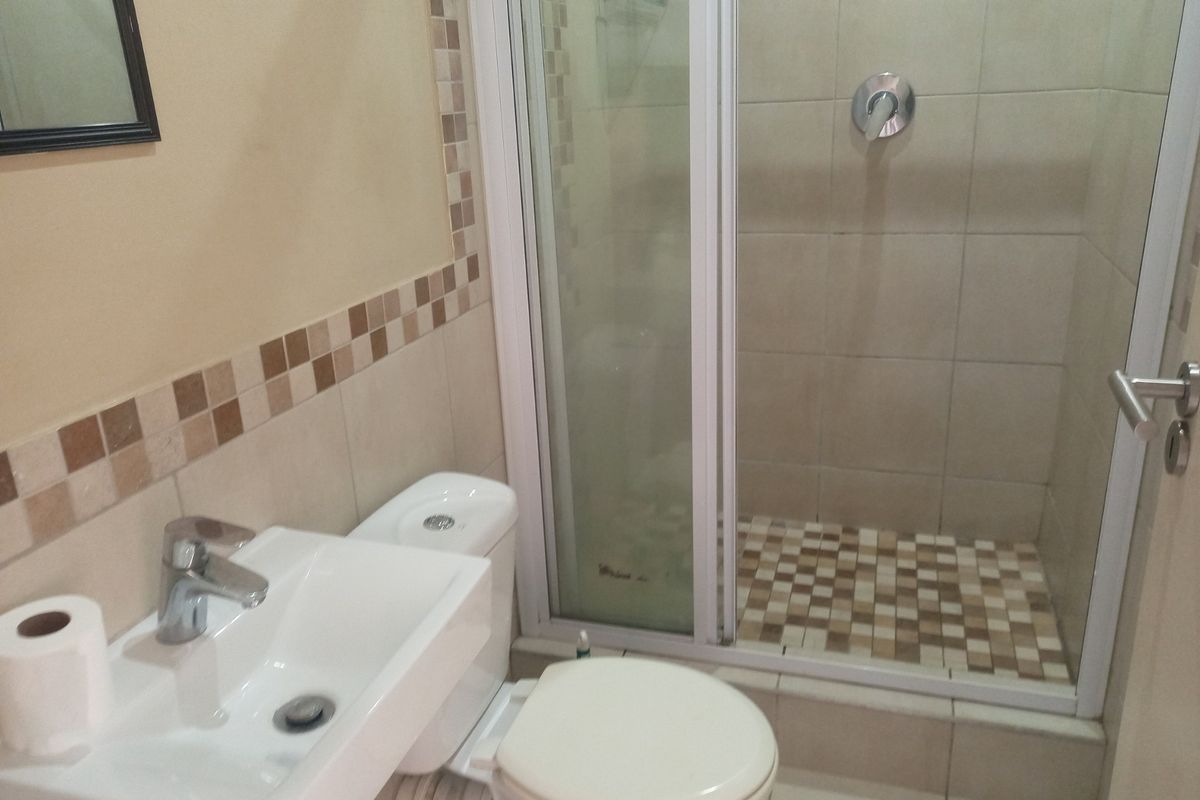 A functional bathroom featuring a shower enclosure, wall-mounted basin, and toilet with neutral tiled finishes.