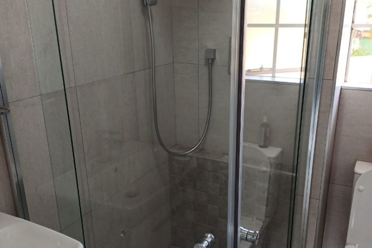 A modern bathroom featuring a glass-enclosed shower with rainfall and handheld shower heads, tiled finishes, a wall-mounted basin, and a toilet.