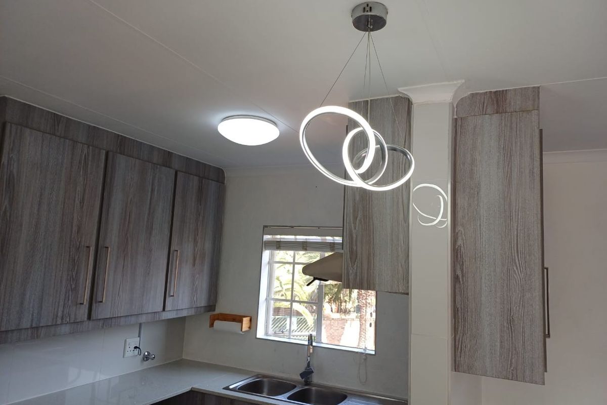 A modern kitchen featuring wood-grain cabinetry, stone countertops, a double basin sink, and contemporary pendant lighting.