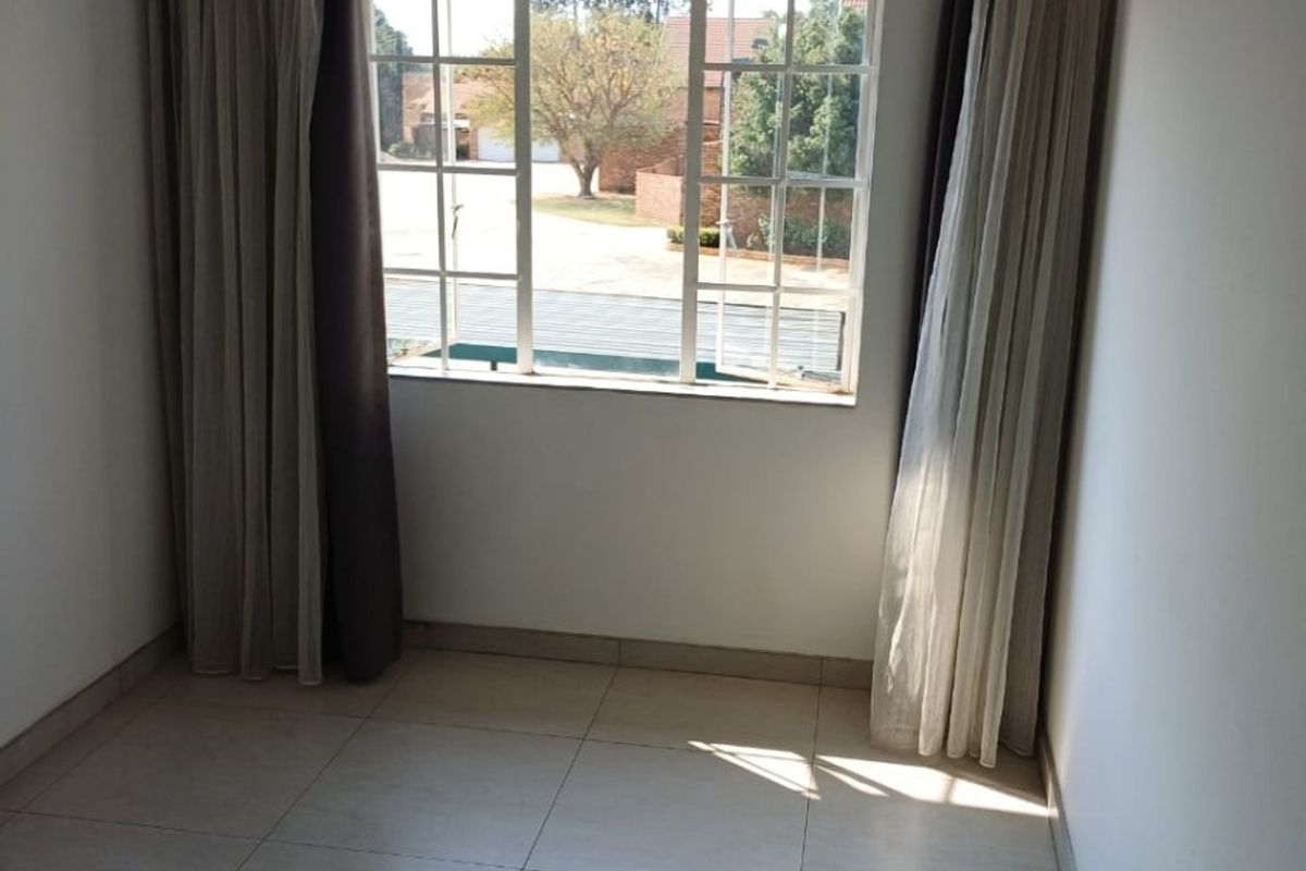 A bright, empty bedroom featuring neutral tiled flooring and a large casement window with installed curtain rails.