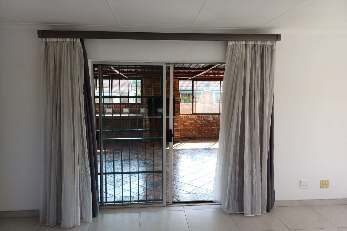 Bright living area featuring tiled flooring and a sliding glass door with security gate, providing direct access to an outdoor patio space.