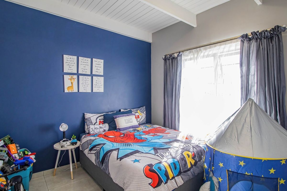 A bright bedroom featuring exposed beam ceilings and tiled flooring, currently utilized as a child's room.