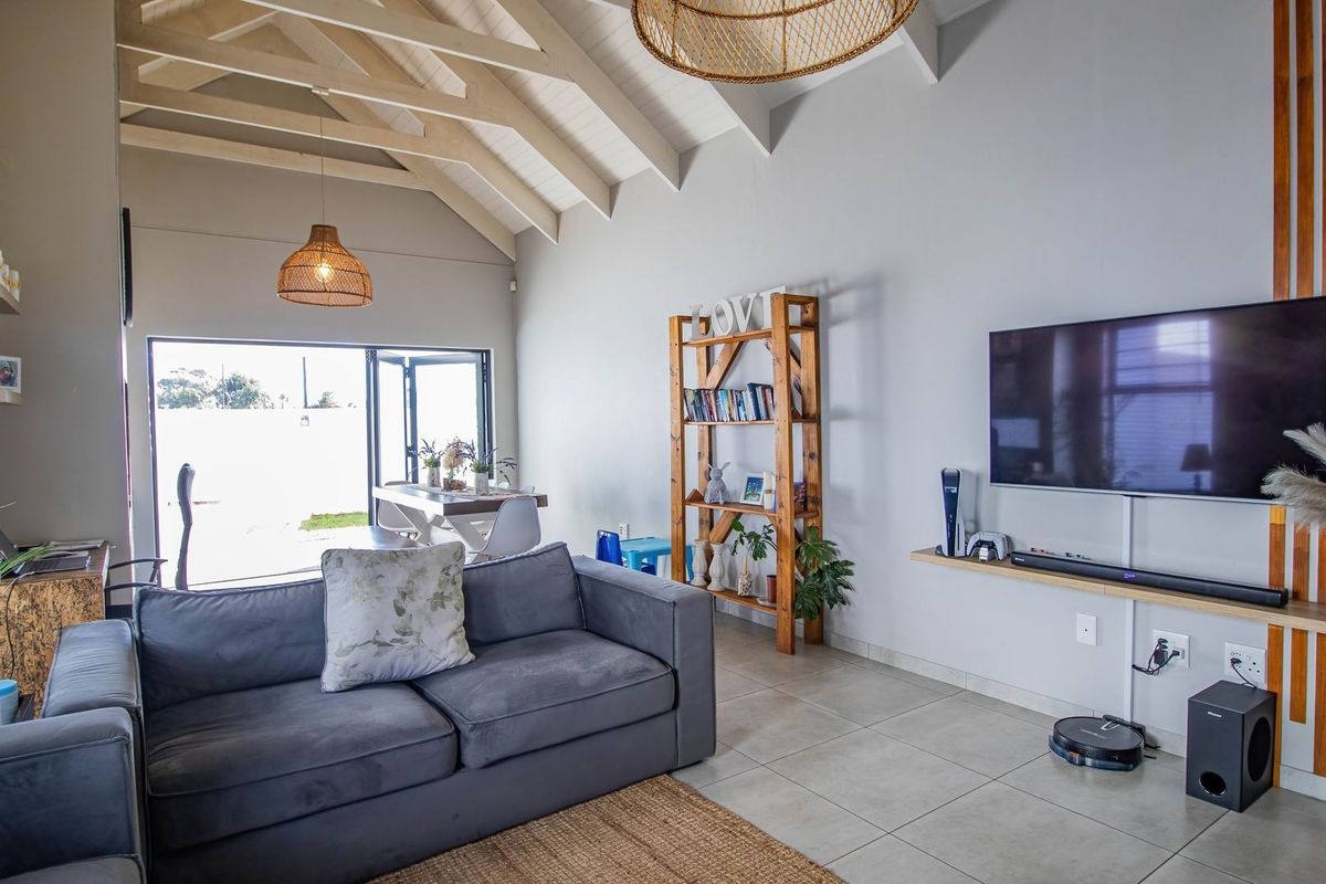 Spacious living room featuring a high vaulted ceiling with exposed timber rafters, tiled flooring, and large bi-fold doors opening to the outdoor area.