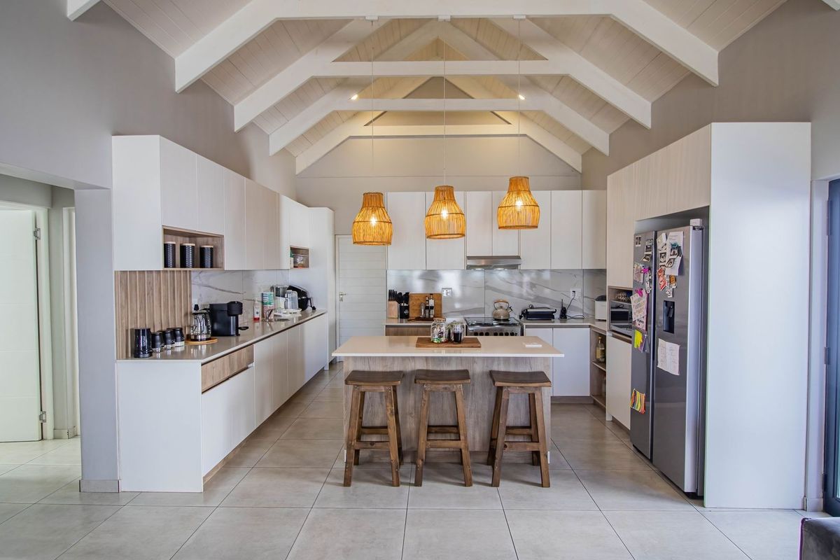 Modern open-plan kitchen featuring white cabinetry, stone countertops, a central island, and a striking vaulted ceiling with exposed timber beams.