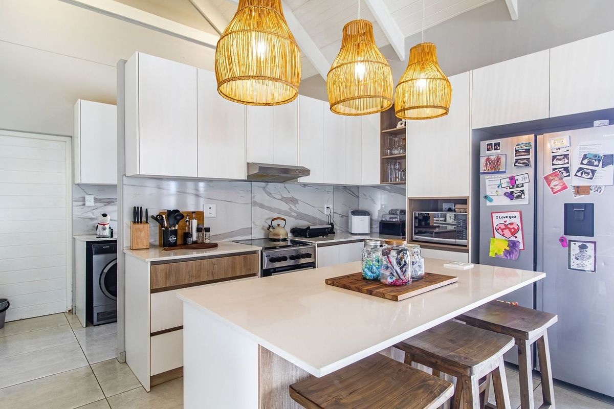Modern kitchen featuring a central island with stone countertops, sleek white cabinetry, marble-look splashback, and vaulted ceilings with exposed rafters.