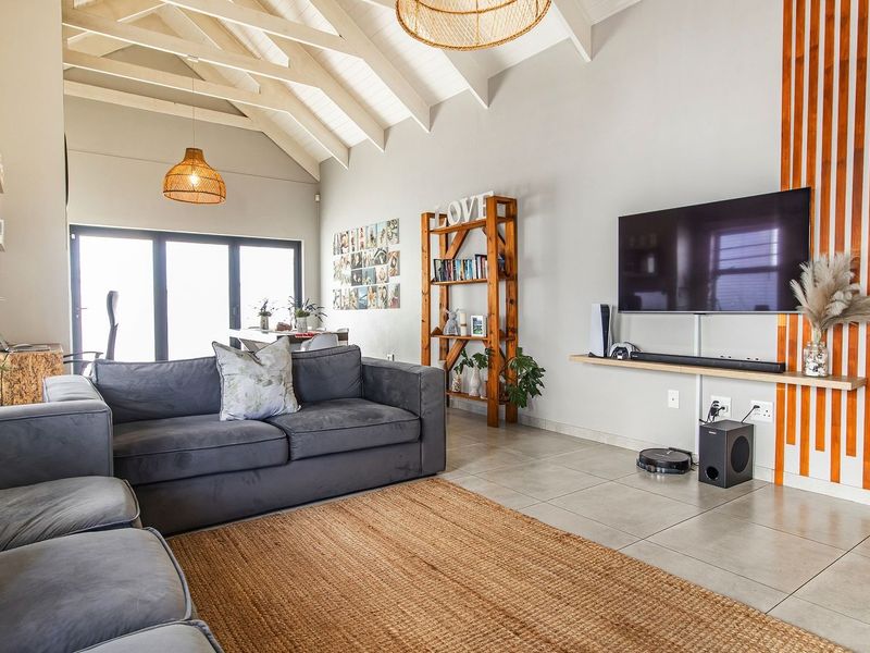 Spacious living room featuring a high vaulted ceiling with exposed rafters, tiled flooring, and a modern timber slat feature wall.
