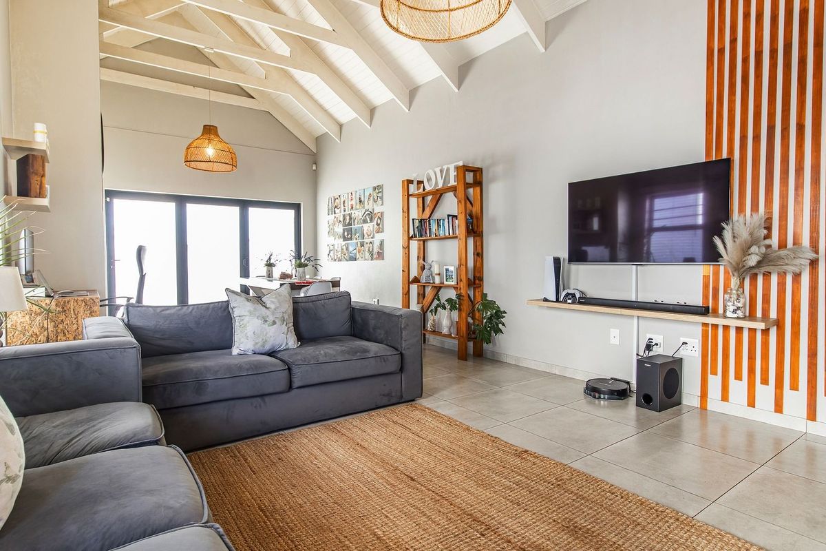 Spacious living room featuring a high vaulted ceiling with exposed rafters, tiled flooring, and a modern timber slat feature wall.