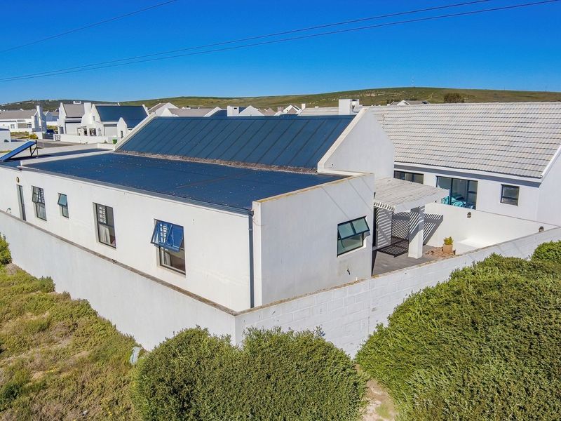 Aerial view of a modern residential property featuring a metal roof with integrated solar panels, a perimeter wall, and a rear pergola.