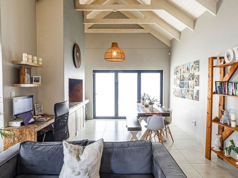 Spacious open-plan living and dining area featuring high vaulted ceilings with exposed timber trusses, tiled flooring, and a built-in fireplace.