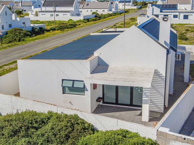 Aerial view of a modern house featuring a paved patio with a pergola, solar panels on the roof, and a secure boundary wall.